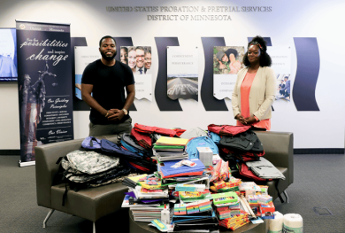 A man and a woman pose in front of the school supplies collected for local school areas.