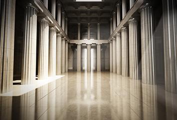 An image of columns inside of a building leading to doors at the end of the hallway.