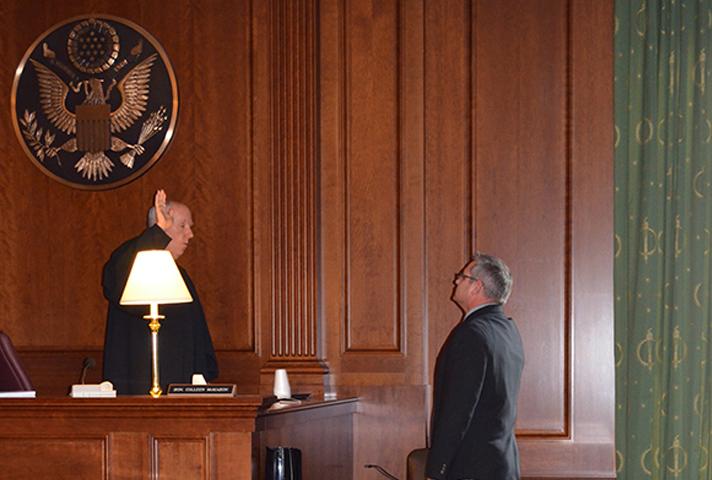 Judge Castel swears in a witness in a dimly lit courtroom. Small table lamps provided the necessary light to conduct proceedings during the week of the storm.