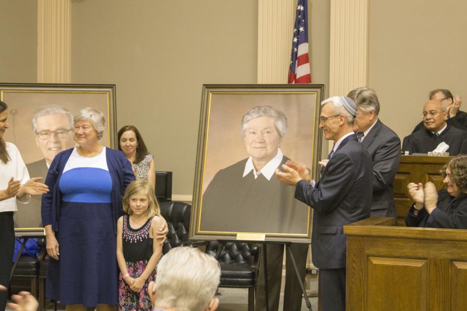 Retired Judge Holly B. Fitzsimmons and her granddaughter stand beside her portrait presented by Alyssa Esposito, a former law clerk for Judge Fitzsimmons, and James Ross Smart Esq. and Patrick A. Klingman Esq., Co-Chairs of the Federal Practice Section at