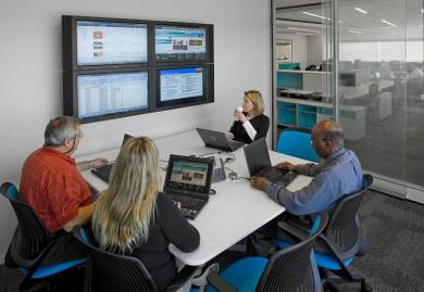 Glass-enclosed meeting rooms can be smaller, while maintaining an open feel. Here, a meeting is held at an office of Accenture, a consulting firm that has assisted on the Integrated Workplace Initiative.