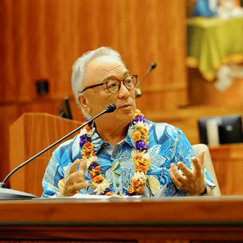 Eric Yamamoto, wearing a blue and white floral shirt and floral lei, discusses the importance of having a federal court vacate Korematsu’s conviction, some 40 years later.