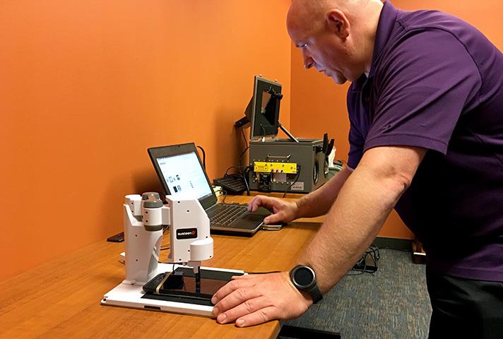 Senior Probation Officer Steve Holmes programs a robotic arm to try to crack a passcode on a locked mobile device at the Eastern District of Missouri's National Forensic Laboratory.