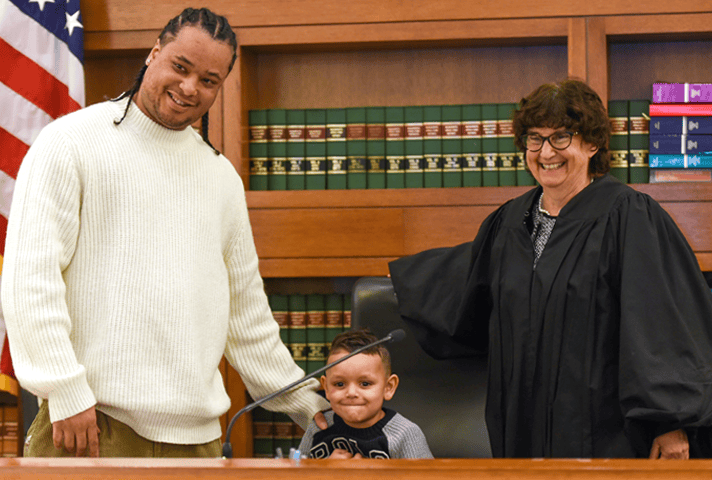 Judge Patti B. Saris in her courtroom with a reentry program graduate and his son.