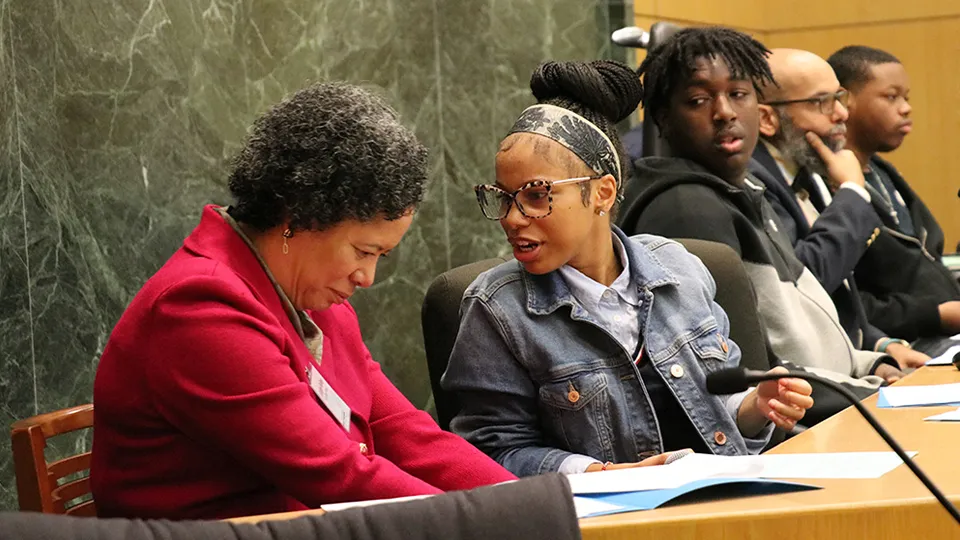 Seated on the bench, U.S. District Judge Angel Kelley, left, confers with a student during oral arguments on the First Amendment at a civics program in a Washington, D.C. courtroom.