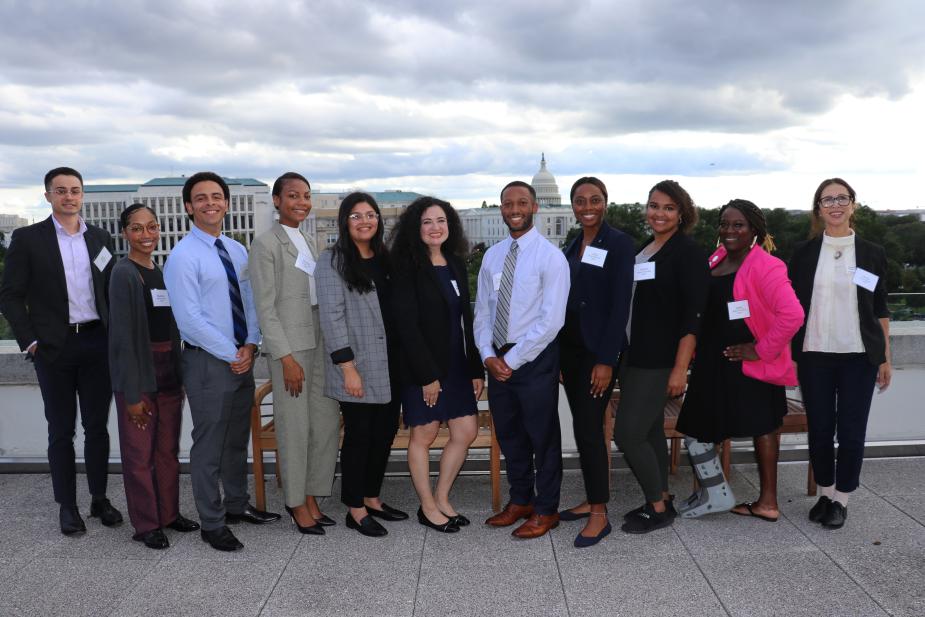 A group of fellows pose at the Thurgood Marshall Federal Judiciary Building with the U.S. Capitol Building behind them.