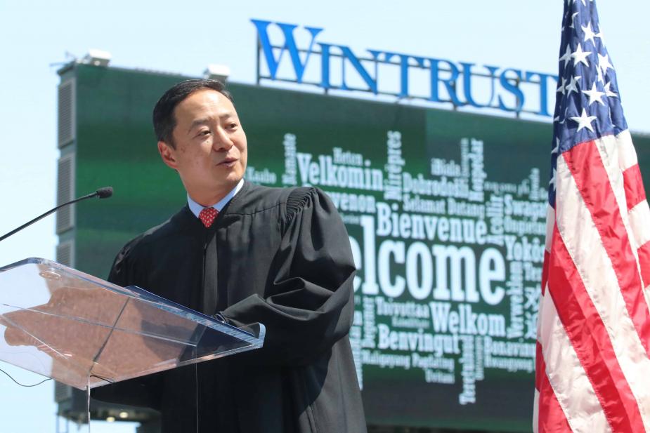 The word “Welcome” displays in several languages on the left field video screen behind U.S. District Judge John Z. Lee of the Northern District of Illinois. Photo credit: Jim Slonoff